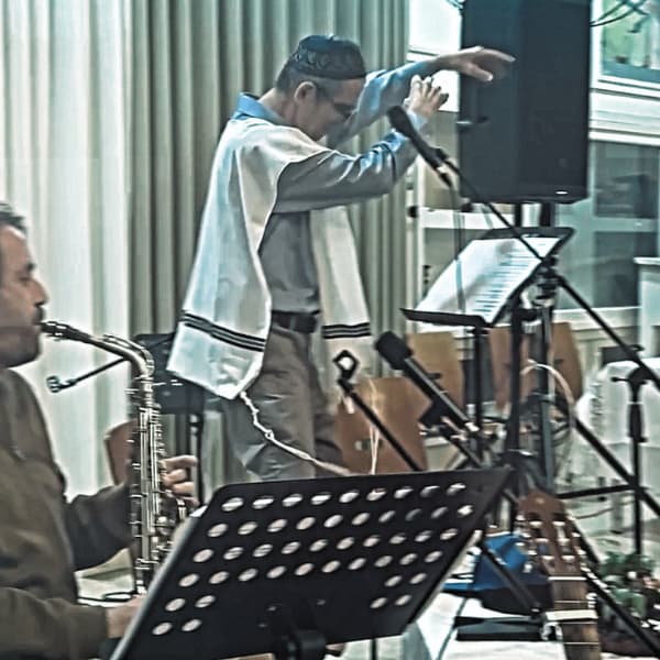 ראובן מודק מנחה את המופע המהפחה הכסידית על הבמה עם נגן סקסופון