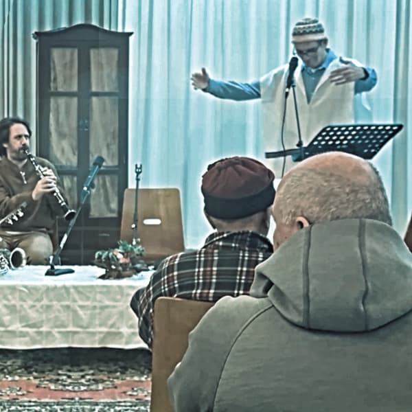 ראובן מודק מנחה את המופע המהפחה הכסידית על הבמה עם נגן קלרינט